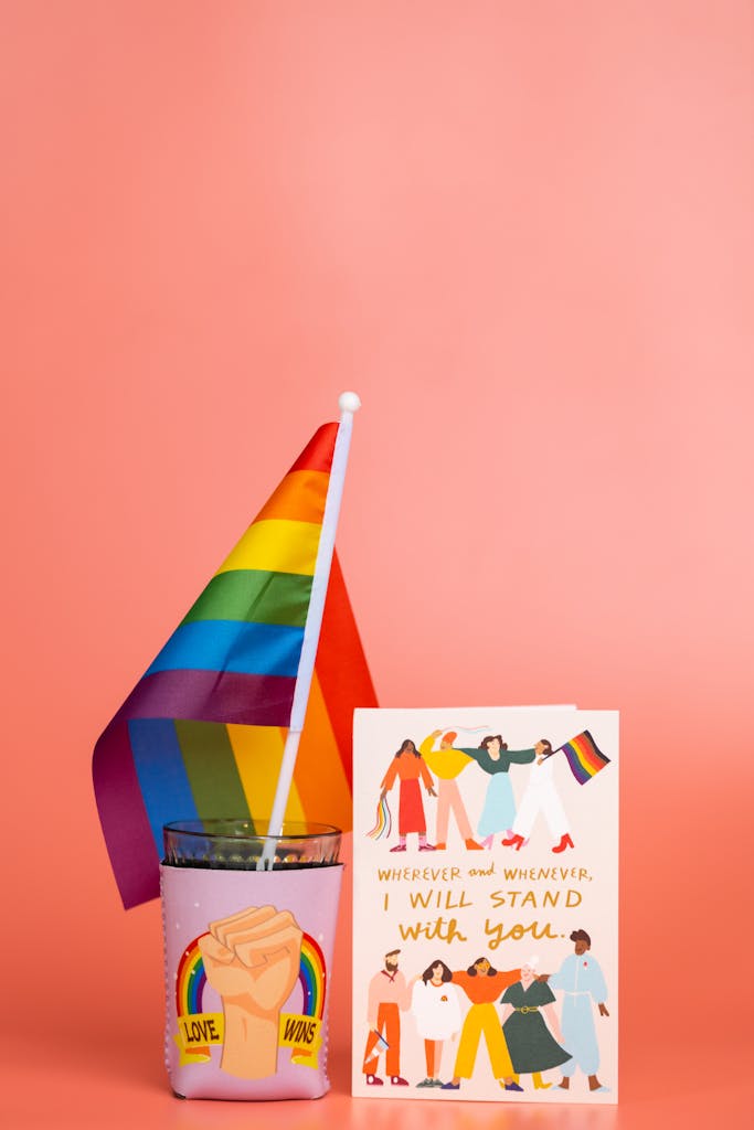 Colorful still life featuring a rainbow flag and supportive LGBTQ message card on a pink backdrop.